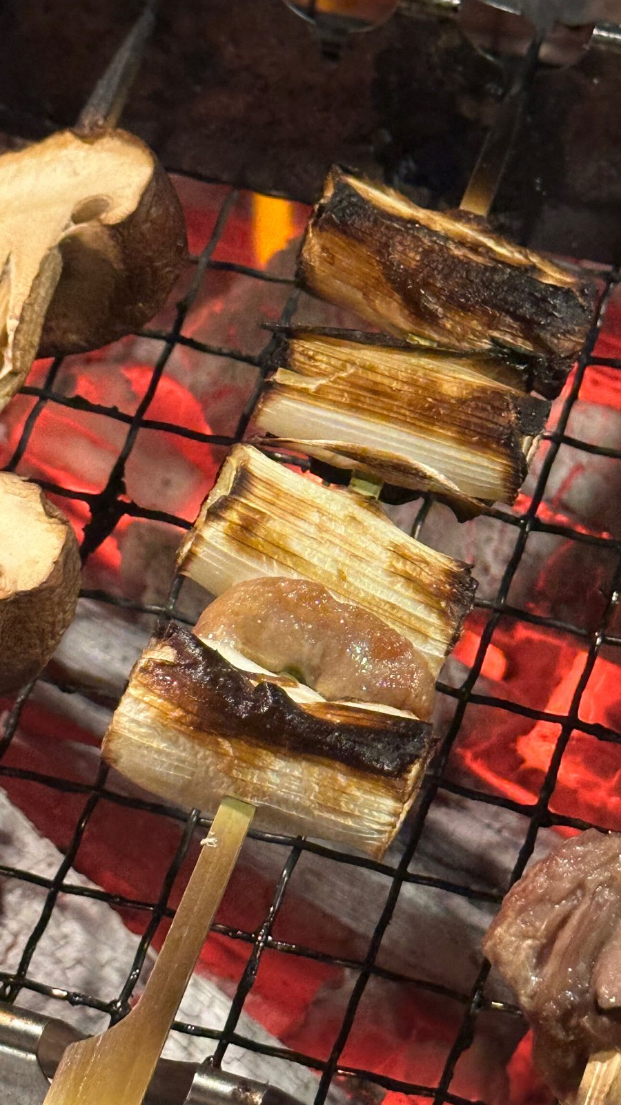 炭火の焼き網の上で焼かれているねぎま串。ネギにこんがりと焼き色がついている